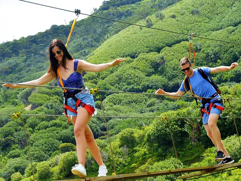 Zipline riders flying over a green valley